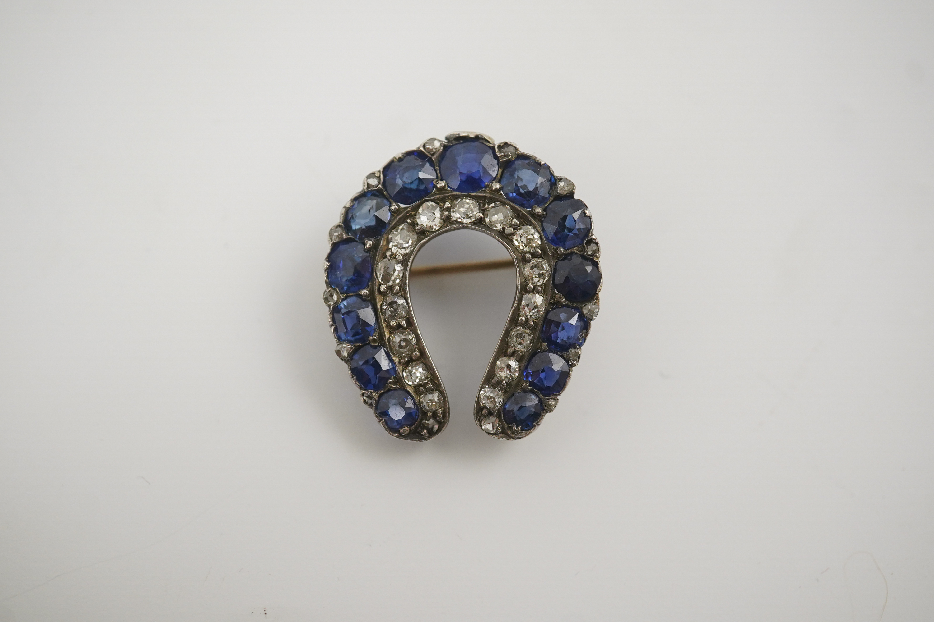 An Edwardian, gold and silver, diamond and sapphire set ‘horse shoe’ brooch